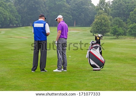 Golfer and caddy on the fairway of a par 4 reading the course guide for club selection.
