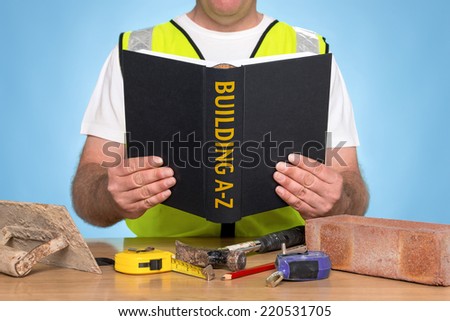 A builder sat at a desk reading a BUILDING A-Z book