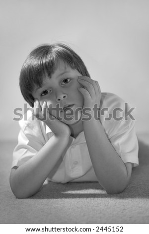 A black & white image of a boy with his head in his hands looking forwards