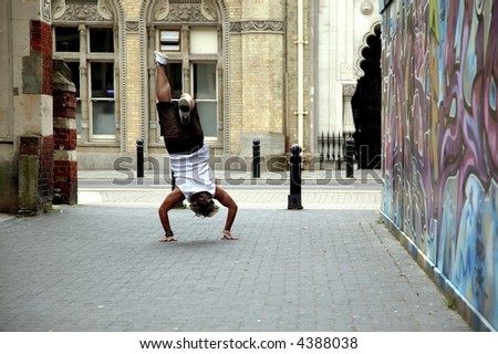 Man in summer attire doing a handstand next to a graffiti wall.