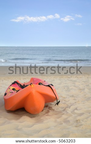 Orange sea kayak on a sandy beach, sea in the background.