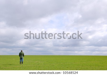 A man standing in a green field under a cloudy sky looking towards the horizon.
