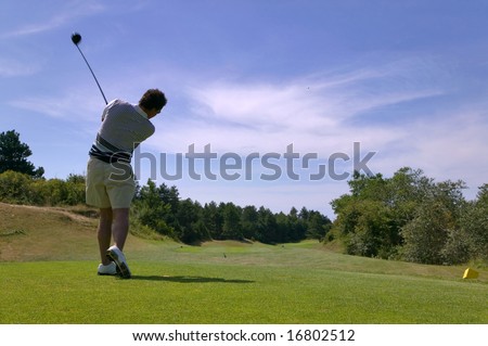 Shot of a male golfer teeing off with the ball in mid air on a bright sunny day, slight motion blur on the club.