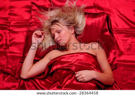 Beautiful blonde woman asleep on red satin sheets