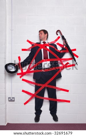 Businessman holding an umbrella and bowler hat stuck to a wall with red tape.