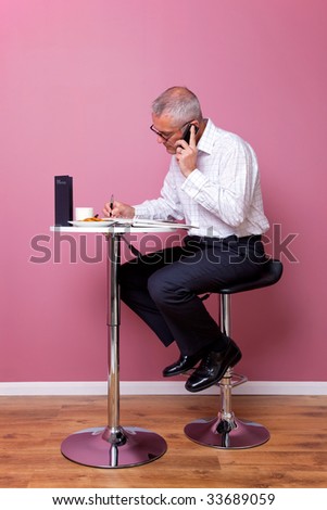 Businessman in smart casual attire sat on a bar stool in a cafe working through his lunch break.