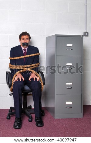 Businessman tied to an office chair with rope, look of fear on his face.