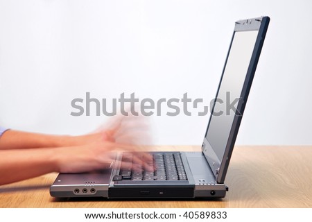 A woman hands typing on a laptop computer keyboard with motion blur to emphasise the speed. Blank screen to add your own message.