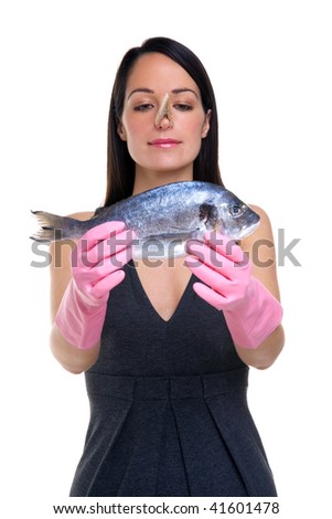 A woman wearing rubber gloves with a clothes peg on her nose holding a fish out in front of her, focus is on her face.