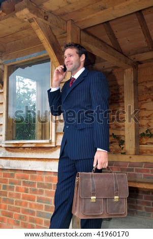 Businessman in his late twenties standing at a rural bus stop talking on his mobile phone