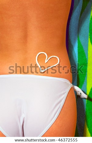 Lower half of a woman sunbathing wearing white bikini bottoms with a suntan cream drawing of a heart on her back