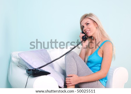 Young blond woman sat in an armchair talking on the telephone
