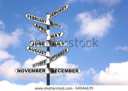 A directional signpost showing the months of the year against a blue cloudy sky.