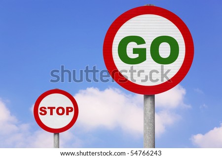 Round roadsigns with GO and STOP on them against a blue cloudy sky.