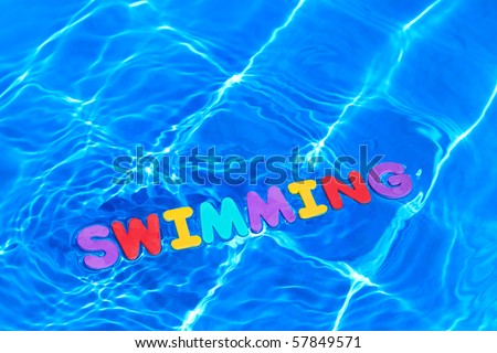 The word SWIMMING made from foam letters floating on the water surface of a pool