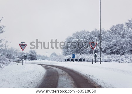 Shot of a road on the approach to a roundabout after a heavy snow fall, Give Way signs