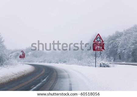 Road with Reduce speed now sign during snow fall of winter 2010