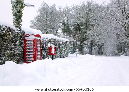 A traditional red English public phone and post box after a heavy snow fall.