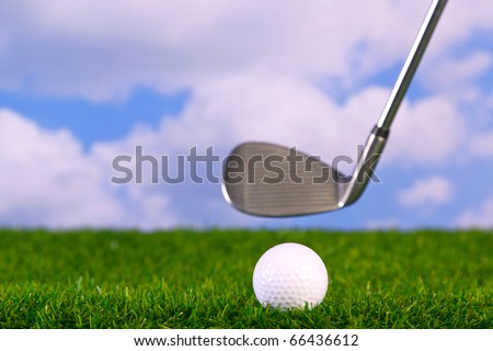 Surface level photo of an iron golf club in mid swing about to hit a ball on the fairway.