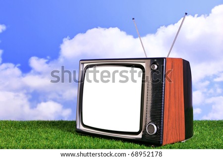 Photo of an old retro TV outdoors on grass with blue sky and white clouds in the background, blank screen with clipping path to add your own content.