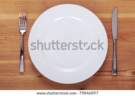 Photo of an empty white plate with knife and fork on a rustic wooden table.