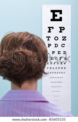 Photo of a woman at the opticians having her eyesight tested using a eye chart to see if she needs glasses.