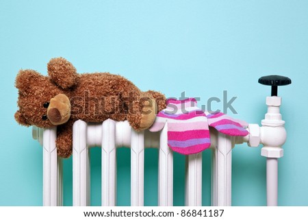 Photo of a childs teddy bear and woolen mittens drying on an old traditional cast iron radiator, good image for winter and childhood themes. The bear is a generic non-brand bear, FYI he\'s called Bob!