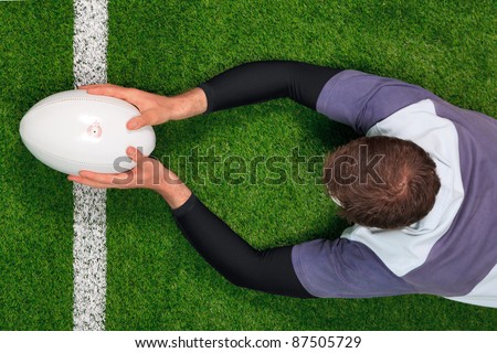 Overhead photo of a rugby player diving over the line to score a try with both hands holding the ball.
