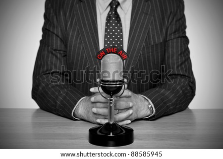 Photo of a news broadcaster sat at a desk and retro microphone with an On The Air illuminated sign converted to B&W retaining the colour of the text and added vignette for a vintage look Photo of a news broadcaster sat at a desk and retro microphone with an On The Air illuminated sign converted to B&W retaining the colour of the text and added vignette for a vintage look