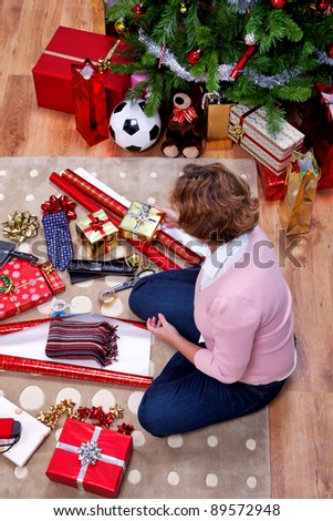 Overhead photo of a woman sat on a rug at home wrapping her Christmas presents. The teddy is generic and is not a brand bear.