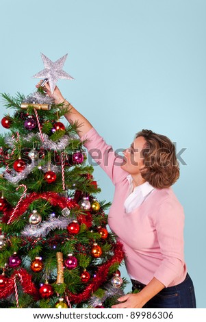 Photo of a woman at home decorating her Christmas tree and finishing off by putting the star on top.