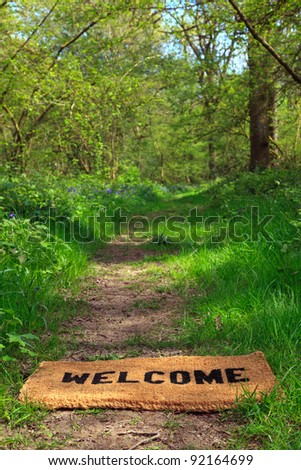 Concept photo of a Welcome doormat on a woodland footpath during springtime in vertical format.