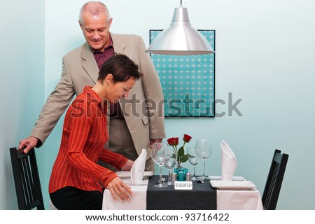 Photo of a mature couple arriving and sitting down at their reserved table in a restaurant
