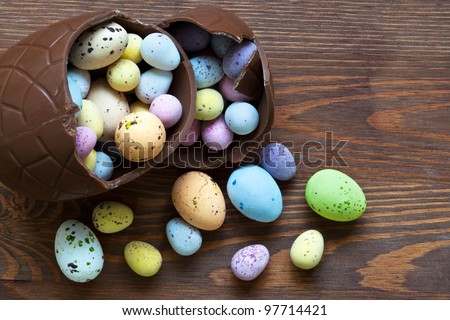 Still life photo of a large broken chocolate easter egg full of mini candy covered eggs in various pastel colours.