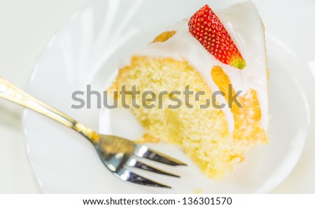 A slice of cheese pound cake coated with sugar glaze and pieces of strawberry