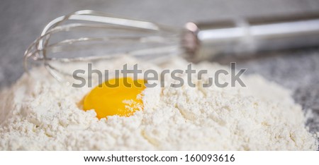 Flour, egg yolk and egg beater on a granite counter surface.