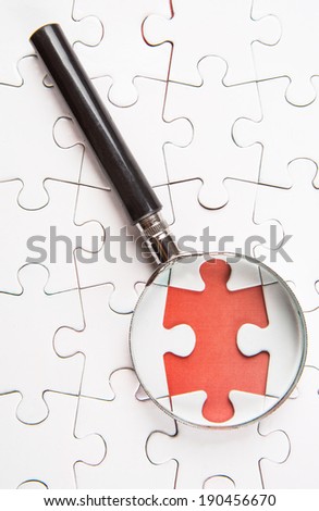 Missing jigsaw puzzle pieces revealing a red surface layer with a magnifying glass