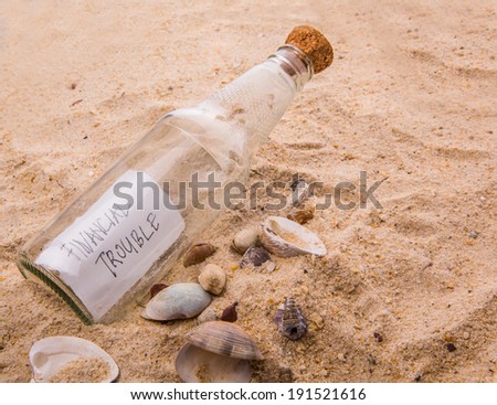 FINANCIAL TROUBLE message written on a piece of paper in a glass bottle on beach sand