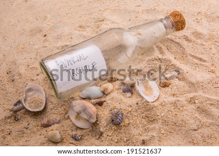 FINANCIAL TROUBLE message written on a piece of paper in a glass bottle on beach sand