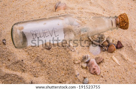 Concept image of BELIEVE message written on a piece of paper in a glass bottle on beach sand