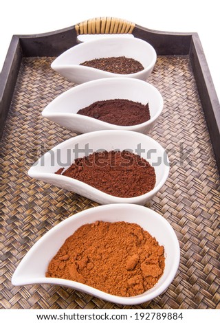 Cocoa powder, ground coffee and dried tea leaves in a white ceramic container in a wicker tray