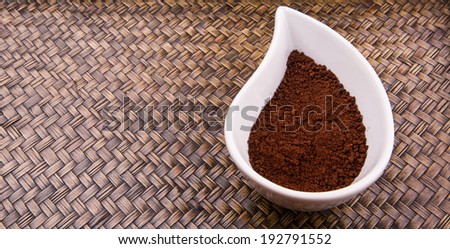 Instant coffee powder in a white ceramic container over wicker background