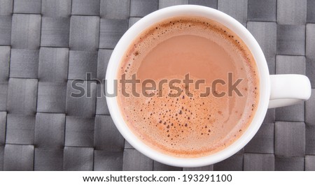 A mug of hot chocolate beverage on a woven table mat.