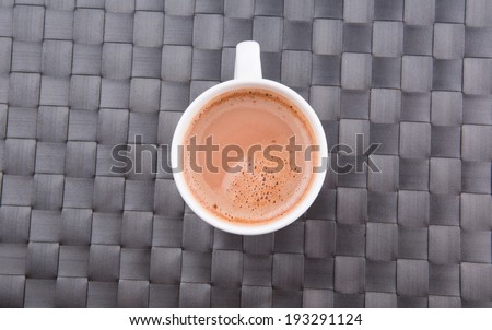 A mug of hot chocolate beverage on a woven table mat.