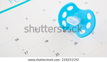 Concept image of pregnancy delivery due date with calendar page and blue pacifier.