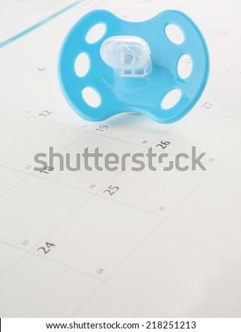 Concept image of pregnancy delivery due date with calendar page and blue pacifier.