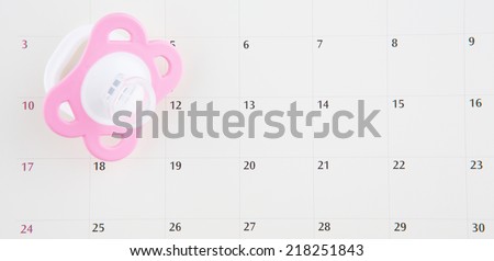 Concept image of baby girl pregnancy delivery due date with calendar page and pink pacifier.