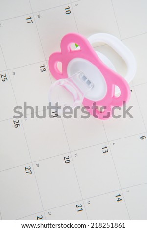 Concept image of baby girl pregnancy delivery due date with calendar page and blue pacifier.