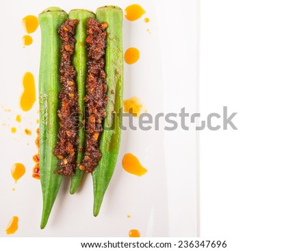 Boiled raw okra or ladies fingers with deep fried crunched chili sambal on white plate over white background