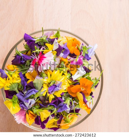 Mix edible flower salad in a glass bowl on wooden cutting board